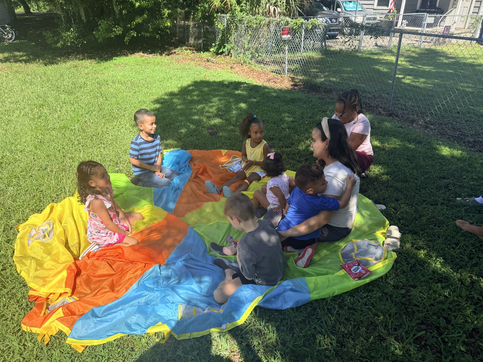 Group of children and teachers playing with a large parachute in the yard