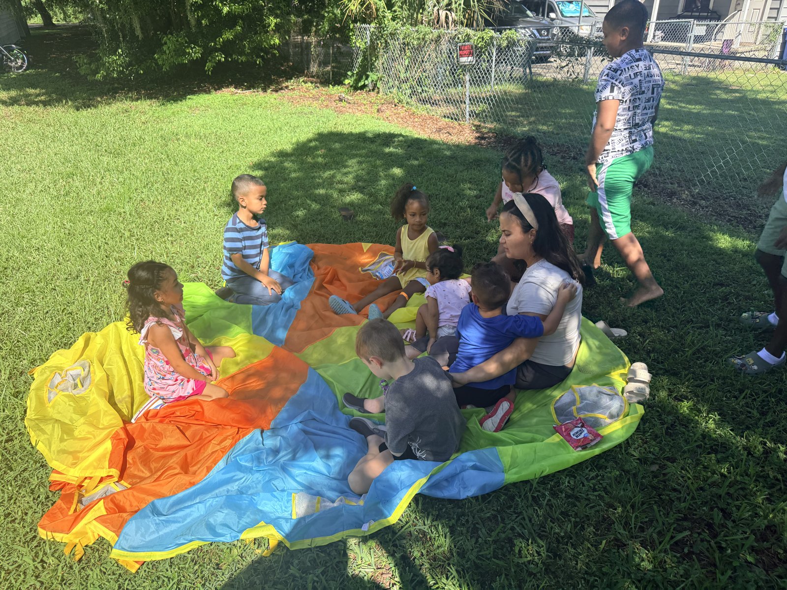 Outdoor group activity with children and teachers gathered around a colorful parachute